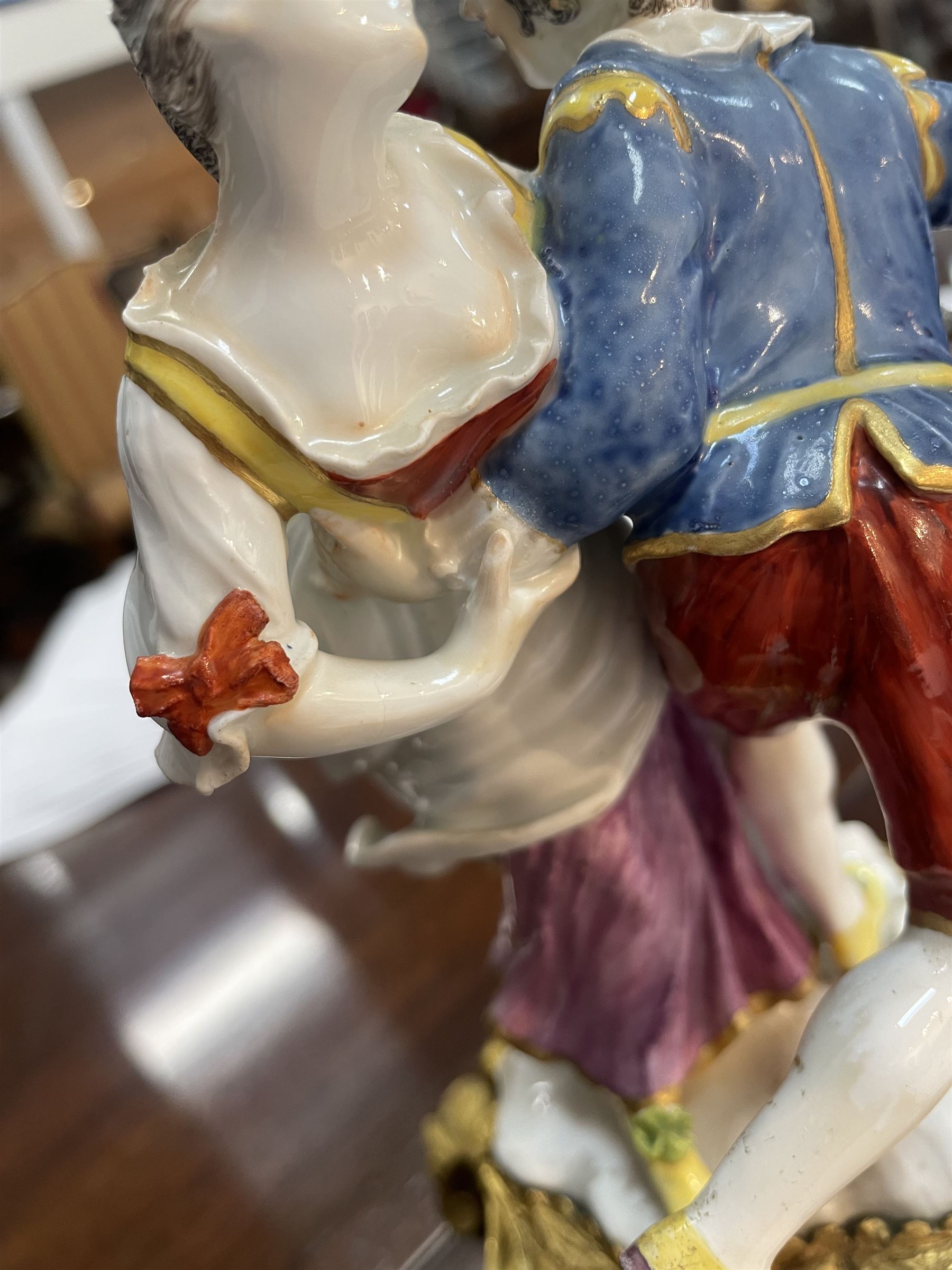 Mid 18th century Meissen figure group, The Tyrolean Dancers, circa 1740, modelled as two swirling figures with their arms linked, he in yellow hat with red rosette, blue jacket, red breeches with red rosette, and yellow shoes with green rosette, she in white blouse with red ribbons, yellow and red bodice, white apron over puce skirt and yellow shoes with green rosettes, her hair fashioned into two plaits secured by red ribbon, upon a shaped mound base, within a scrolling gilt metal mount, with blue crossed swords mark to base, overall H19cm
