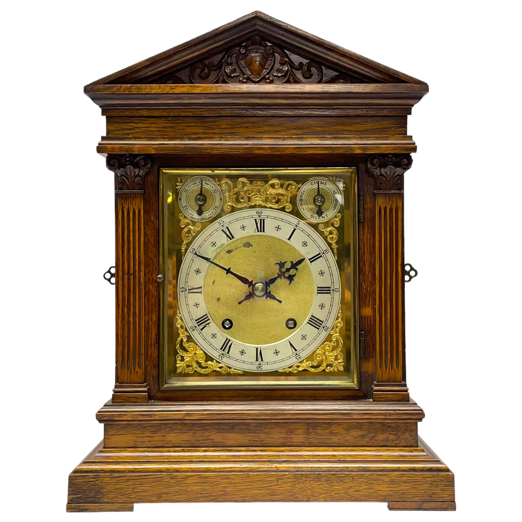 Winterhalder & Hofmeier- German 8-day oak cased mantle clock, in an architectural styled case with a gable pediment and recessed carving to the tympanum, square brass dial flanked by carved reeded pilasters and capitals, with open carved silk backed sound frets on a shaped plinth with padded feet, brass dial with cast spandrels and silvered chapter, Roman numerals, minute track and stylised gothic hands, conforming chime/silent and pendulum regulation dials, twin train going barrel movement with quarter-hour striking on two coiled gongs and the hours on one.
With pendulum.