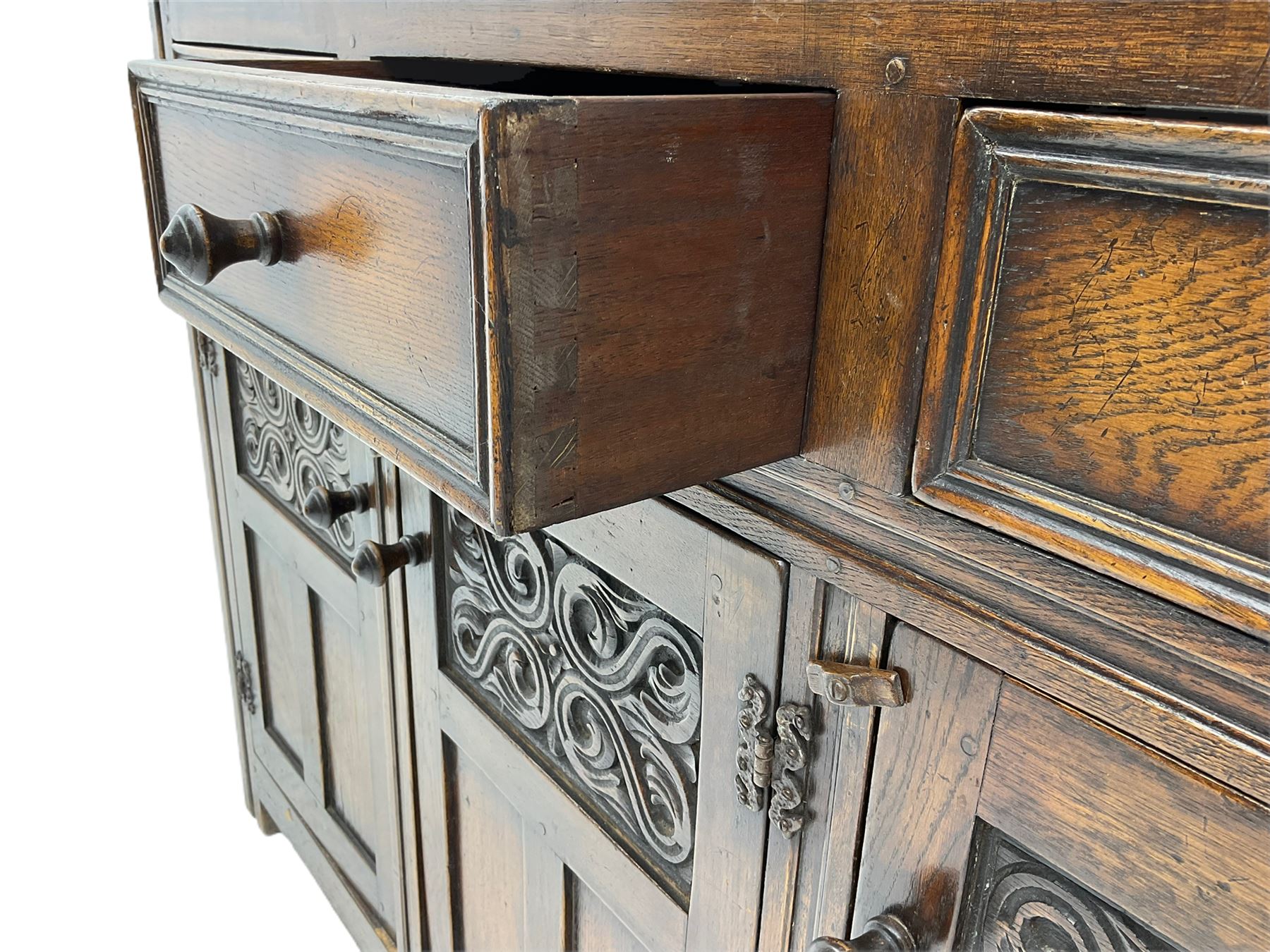 20th century carved oak court cupboard, s-scroll carved frieze over panelled cupboard door carved with arch, lobe and scroll carved cup and cover supports, fitted with three drawers and three cupboards below