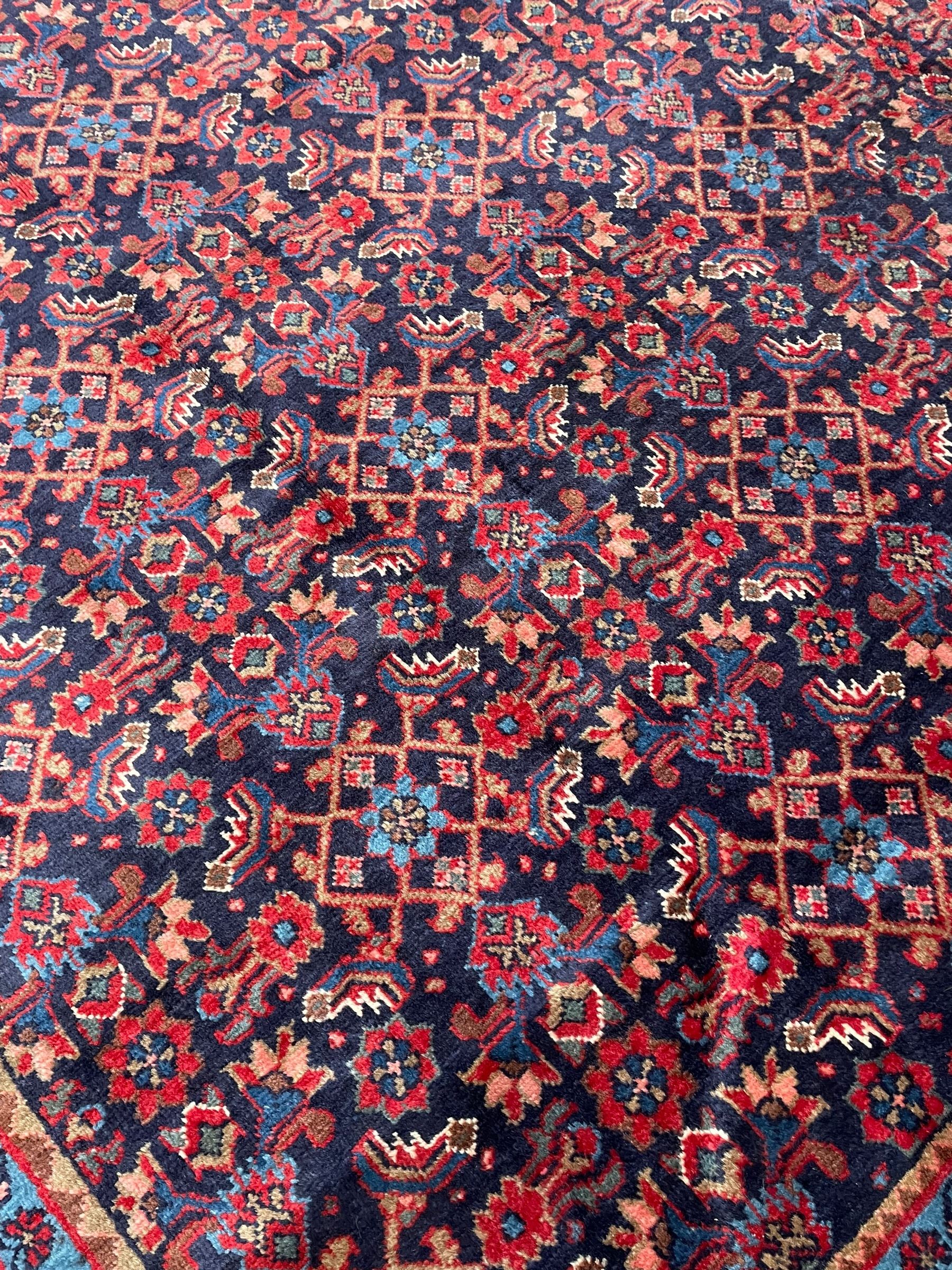Persian indigo ground rug, the field decorated all over with floral Heratti motifs, crimson border with trailing stylised flower heads, within guard stripes
