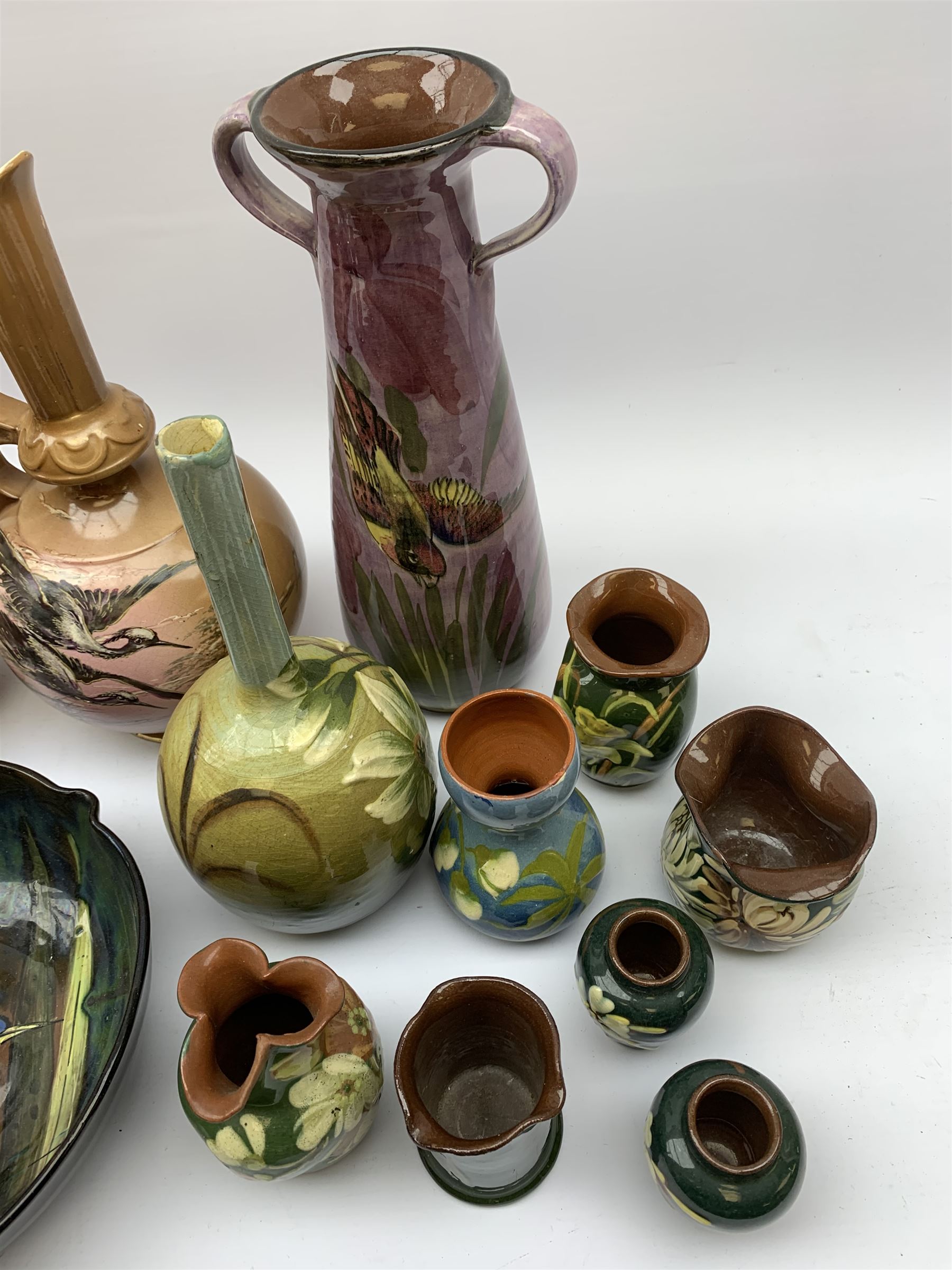 Collection of Devon pottery all having floral slip decoration and include Aller Vale, Watcombe, possibly some Longpark, and other unmarked pieces, tallest H25cm together with a pair of T. Forester jugs hand-painted with cranes and two further Devon pottery pieces, both hand-plated with birds 