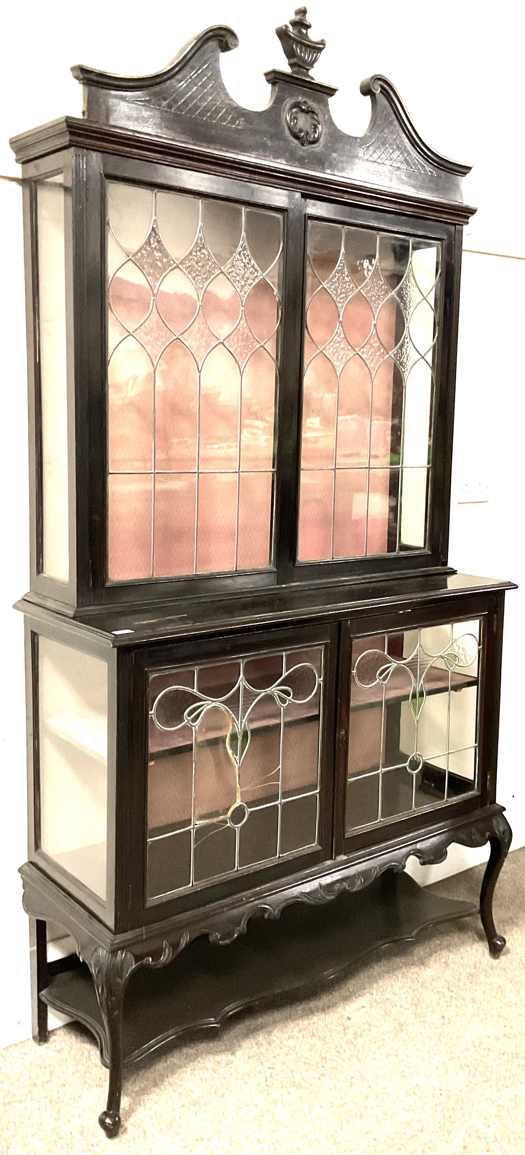 Late 19th century mahogany Empire style display cabinet, swan neck pediment and carved urn finial over two lead glazed doors enclosing two shelves, two glazed doors under, raised on cabriole front supports