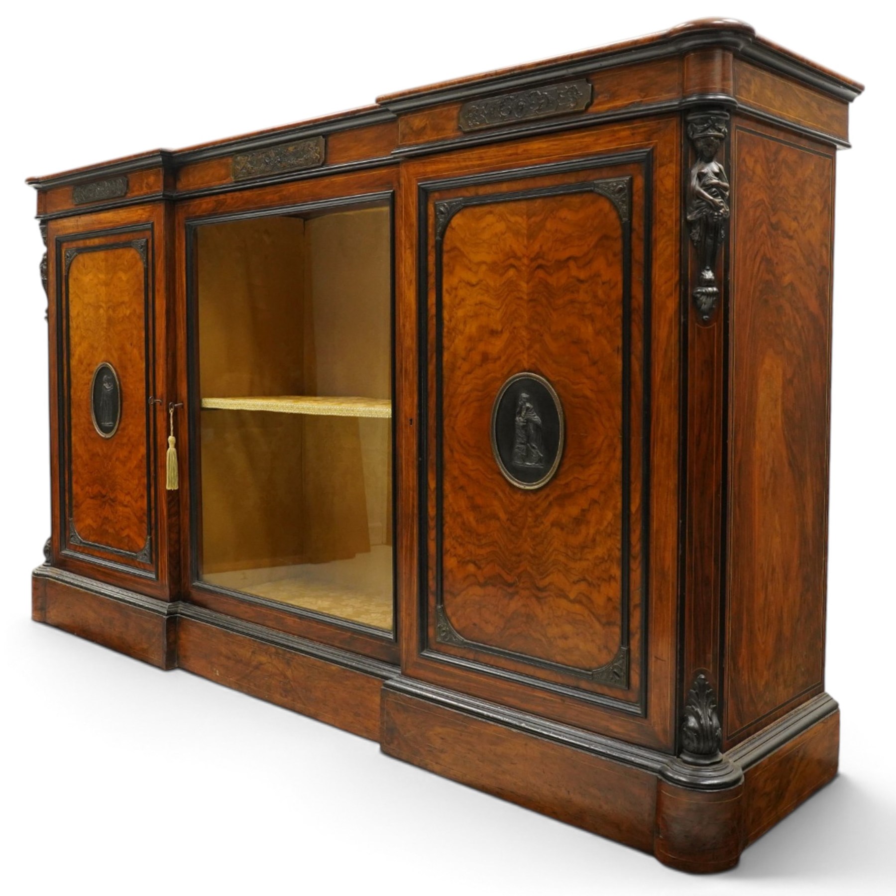 Lamb of Manchester (est. 1843) - Victorian Aesthetic Movement inlaid figured and burr walnut inverted-breakfront credenza, the shaped rectangular top with ebony banding and boxwood stringing, the frieze applied with bronze mounts decorated with foliate and scroll motifs, fitted with central glazed door flanked by panelled doors with central oval metal plaques depicting Classical Muses with lyre, the flanking canted uprights applied with caryatid maidens holding torches, acanthus terminal over skirted base