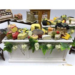 Collection of miniature dolls house grocery shop furniture and produce, comprising glazed corner counter with brass style cash register, shelved preserves unit, pies, cheese board and trays of meats, pair of white cheese counters, biscuit display with six tins, glazed preserves cabinet, pair of shop chairs and four further cheese boards complete with grapes and label flags