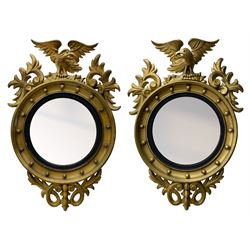 Pair of Regency period giltwood convex wall mirrors, moulded circular frame decorated with spherical mounts surmounted by a carved eagle with spread wings, foliage scroll carved upper and lower brackets, reed moulded and ebonised slip enclosed convex mirror plate 