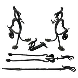 Wrought metal firedogs or andirons, in the form of winged dragons with gaping jaws and projecting tongues, scrolled rear support and extending shaped pad feet; together with matching fireside tongs, poker and tool rest 