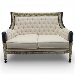 20th century Louis XVI style settee, upholstered in cream fabric with buttoned back and arms, and plain seat cushions, the shaped and black painted frame with entwined foliate detail and gilt flower heads, upon column legs with bun feet