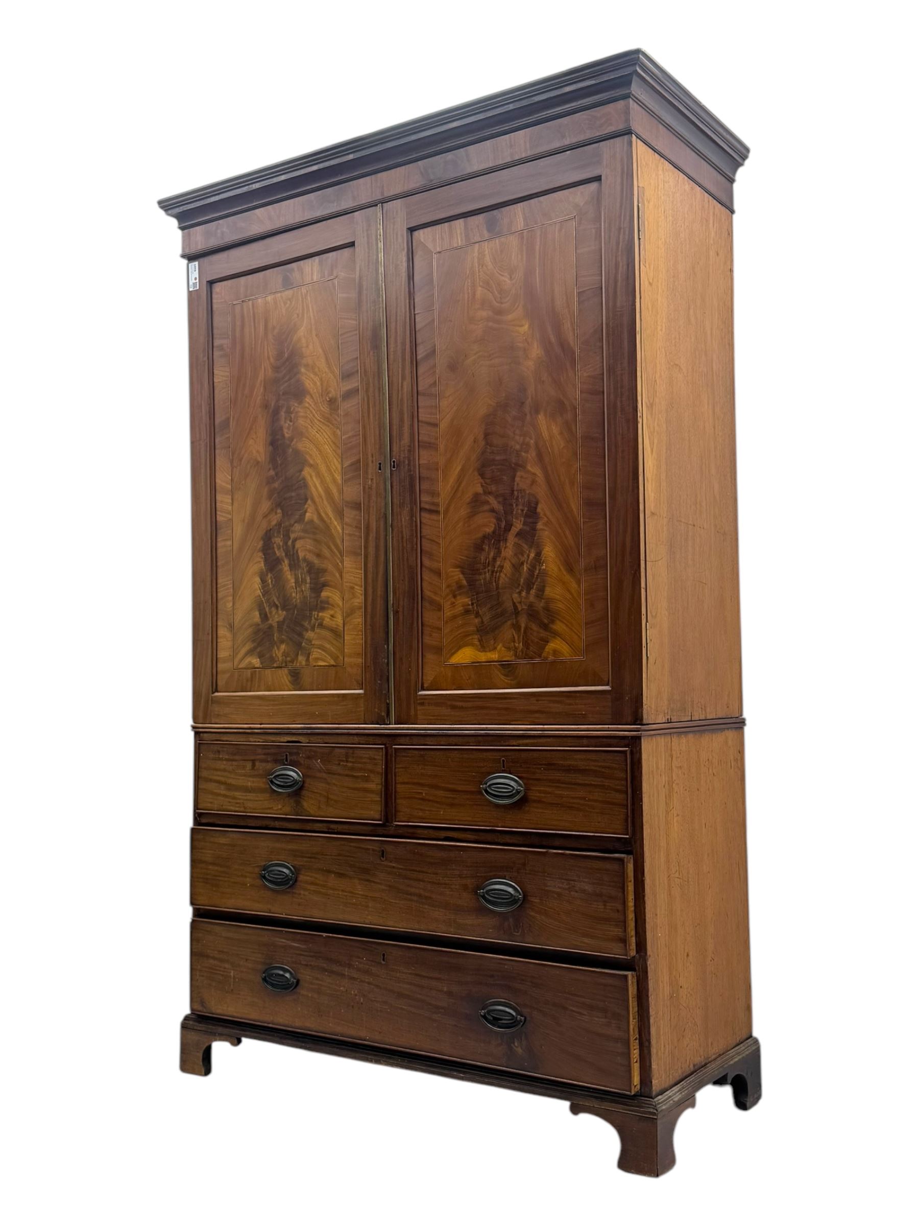 Early 19th century mahogany linen press cupboard, projecting moulded cornice over figured frieze, two panelled doors enclosing shelves, fitted with two short and two long cock-beaded drawers, on bracket feet 