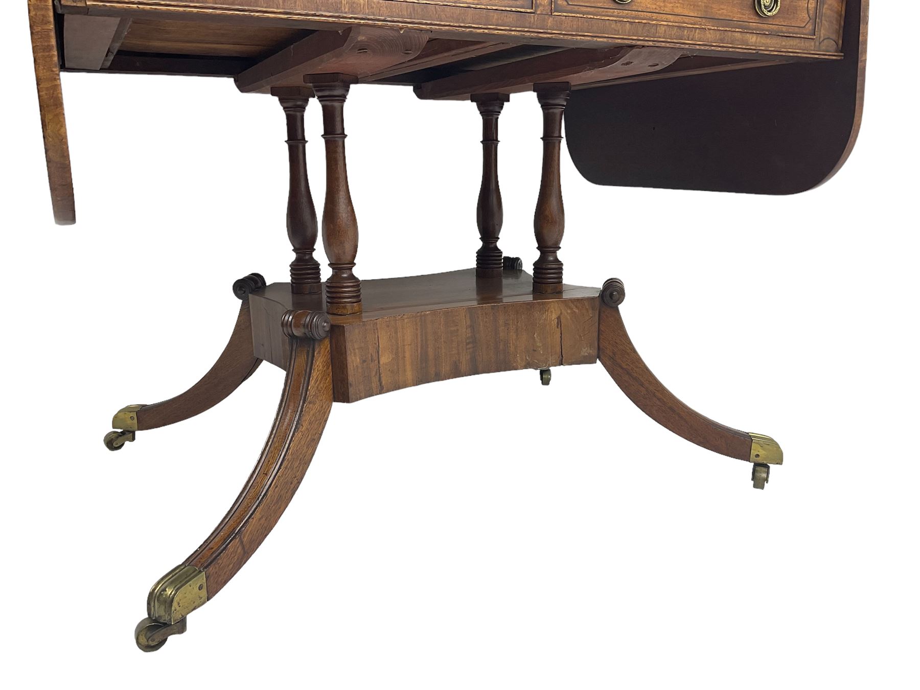 Regency period mahogany drop-leaf sofa table, rectangular top fitted with two cockbeaded drawers with ebony stringing, raised on turned columns united by quadrupod base, the sabre supports terminating in brass cups and castors