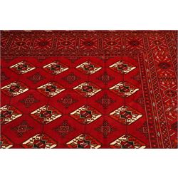Turkmen hand-knotted carpet, deep crimson ground field, with an all-over lattice of repeating diamond guls, each enclosing angular cruiform motifs, and stylized tribal devices, interspersed with smaller geometric ornaments, main border decorated with repeating geometric motifs and stylized tribal elements, flanked by narrow guard stripes, with cotton fringe ends 