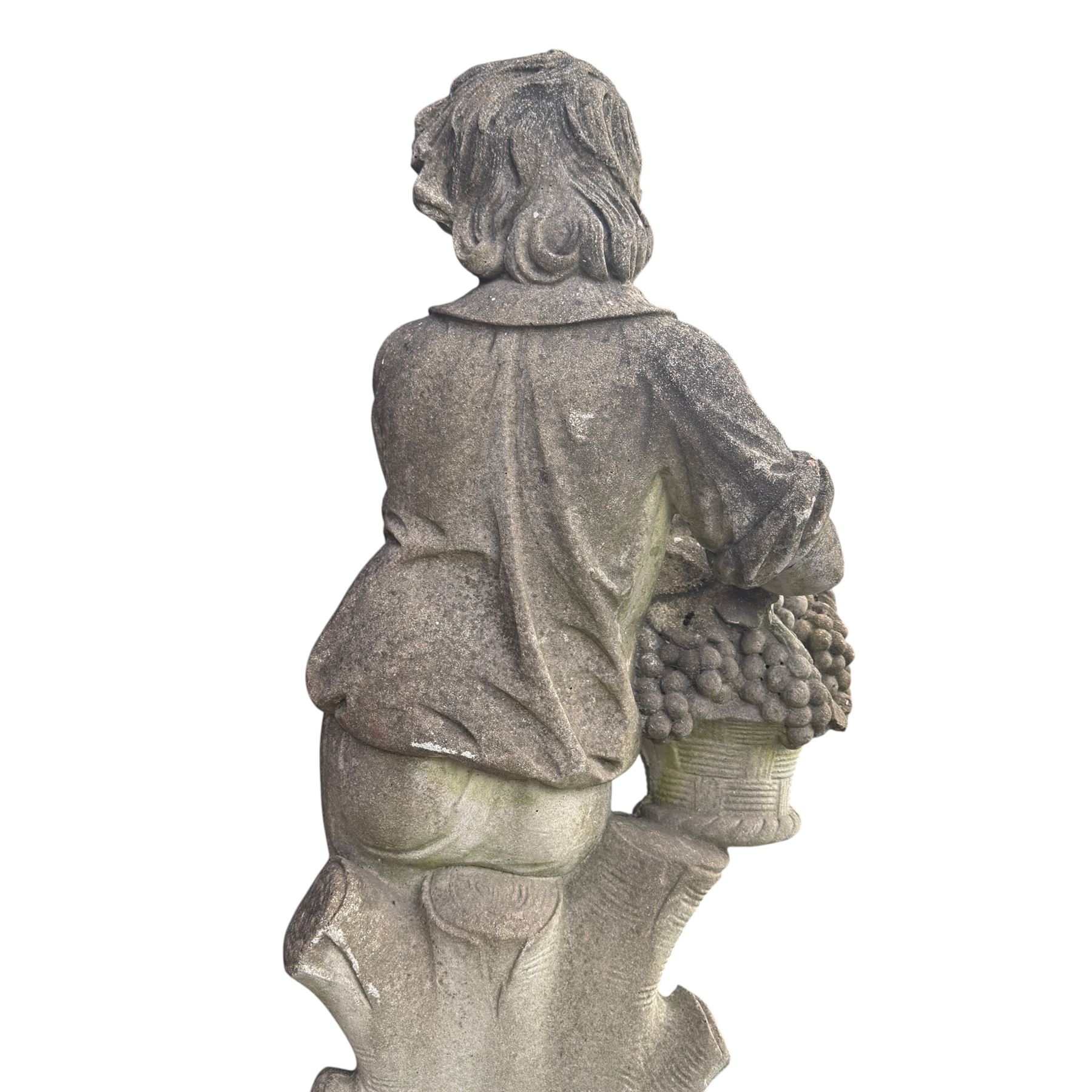 Haddonstone - weathered cast stone garden statue of a boy holding a basket of grapes, modelled with curled locks of hair wearing a tunic and breeches leaning against a naturalistic tree stump, on square base