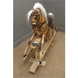  Victorian style wooden rocking horse with stained and dappled carved sectional body, horsehair mane and tail, leather bridle and saddle with iron stirrups, and forward and backward action on stripped pine refectory style base W111cm H102cm  