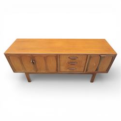 G-Plan - ‘Brasilia’ teak sideboard, rectangular top with moulded edge above a central bank of four drawers flanked by cupboard doors with carved sculptural handles, raised on tapering supports

