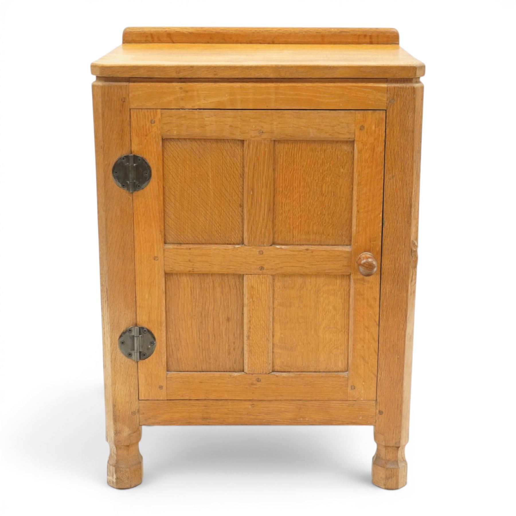 Mouseman - adzed and panelled oak bedside cupboard of small proportions, raised back over rectangular canted top, fitted with single panelled cupboard door with chamfered rails and turned knob handle, enclosing single shelf, raised on octagonal feet,  carved with mouse signature, by the workshop of Robert Thompson of Kilburn
