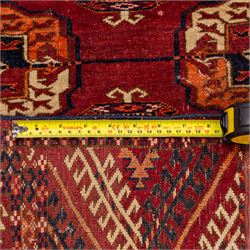 Vintage Bokhara hand-knotted rug, madder field woven in rows of octagonal Tekke guls arranged in vertical columns, each enclosing angular cruciform devices and tribal motifs, divided by narrow indigo lines, within multiple geometric borders incorporating stepped lozenges and latch hook devices, with cotton fringe ends 