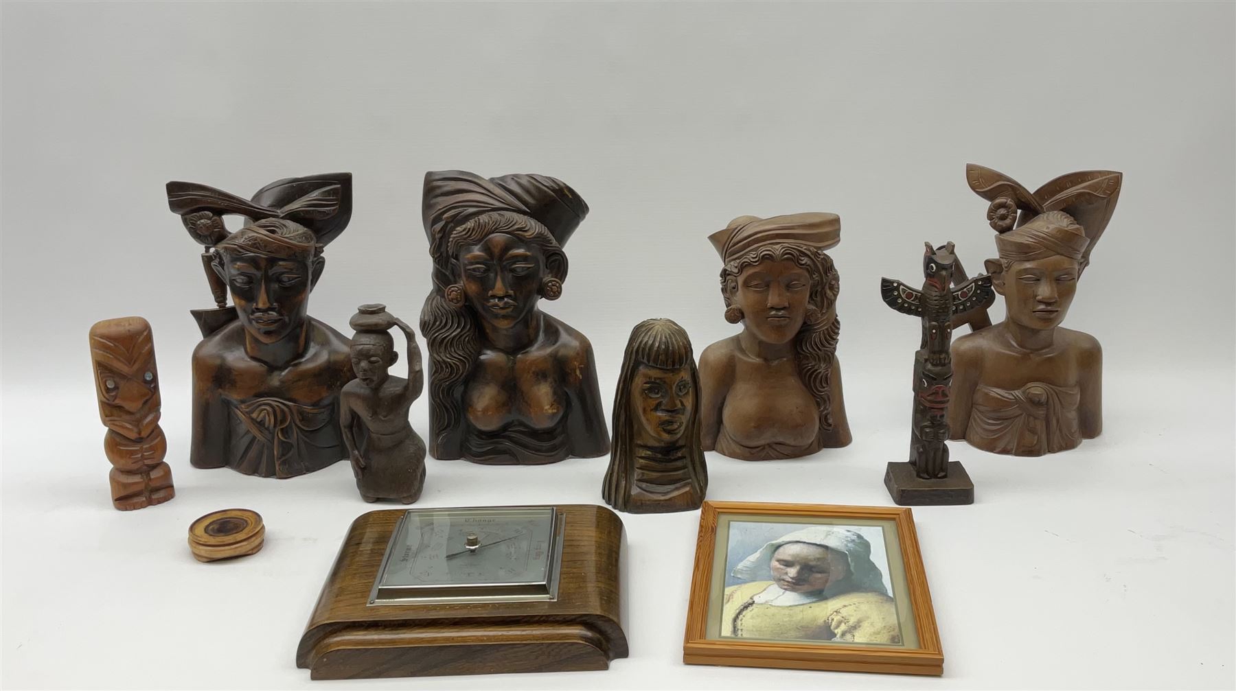 Two pairs of Balinese carved wooden bust figures of a man and woman, with elaborate head dresses, along with other wooden carved figures, a small barometer and a framed print. 