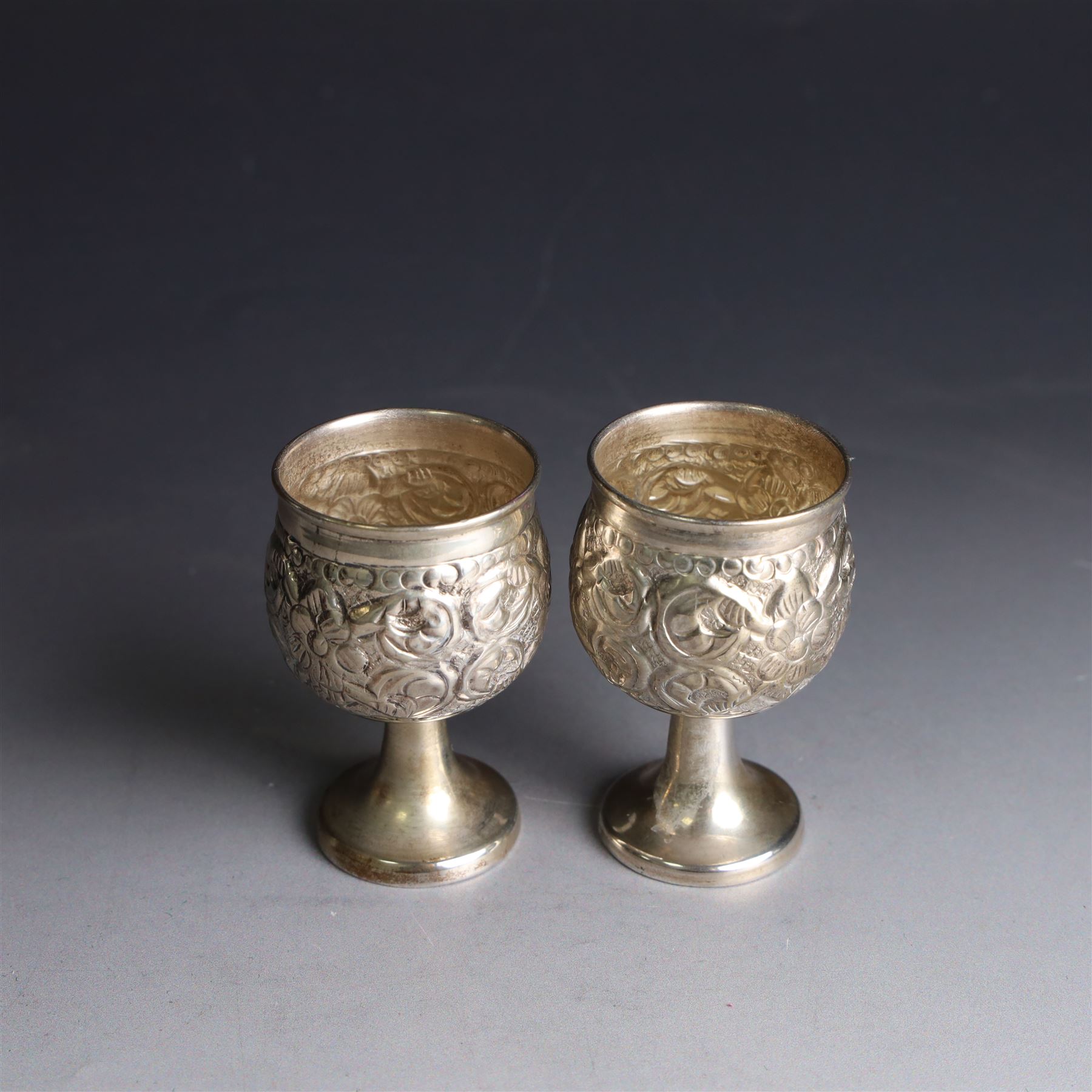 Pair of miniature Indian silver goblets, with embossed floral and foliate decoration, H6.5cm