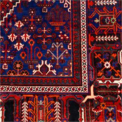 Central Persian Joshagen hand-knotted carpet, madder-red field with a central stepped lozenge medallion and densely filled with stylized geometric floral and tree motifs arranged in a repeating lattice enclosed by indigo spandrels and a broad navy border of angular palmette and vine ornament, flanked by multiple guard stripes, cotton fringe ends 