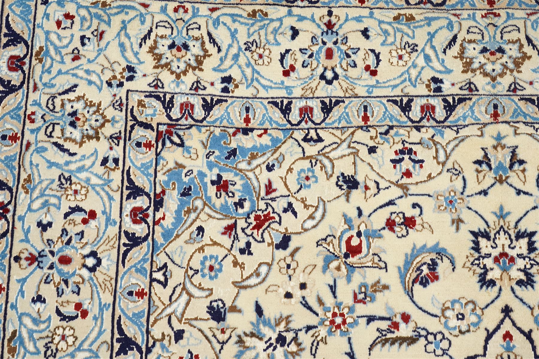 Central Persian Nain hand-knotted rug, ivory field with central medallion in tones of indigo and blue, issuing vinery, palmettes and floral sprays with conforming spandrels, dark blue main border of floral vinery and stylized palmettes, framed by multiple guard borders, with cotton fringe ends 