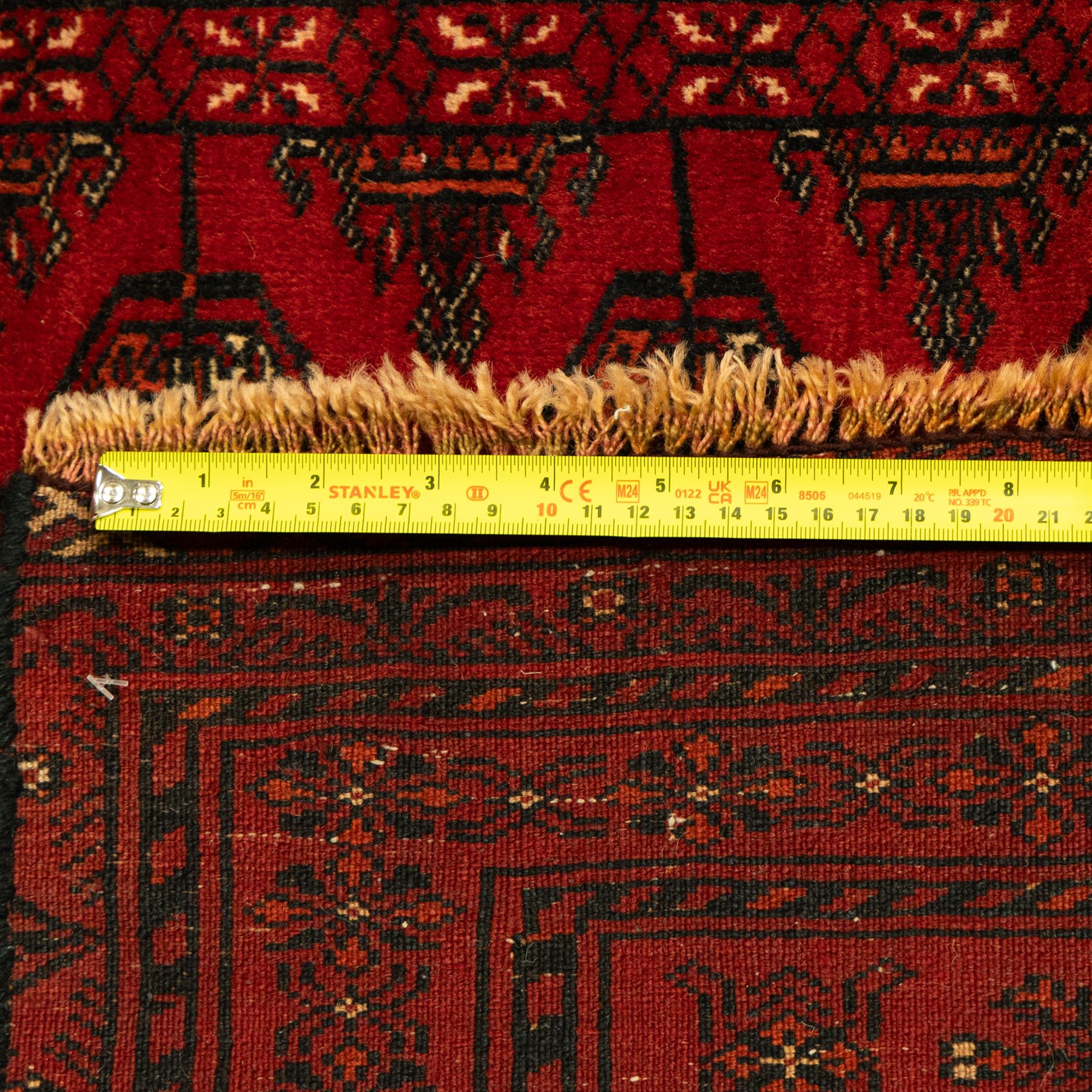 Turkman hand-knotted carpet, deep red ground, with an all-over field of repeating gul motifs arranged in rows, enclosed by multiple red geometric borders with stylised flowerheads and hooked motifs, flanked by narrow patterned guard stripes, with wool fringes