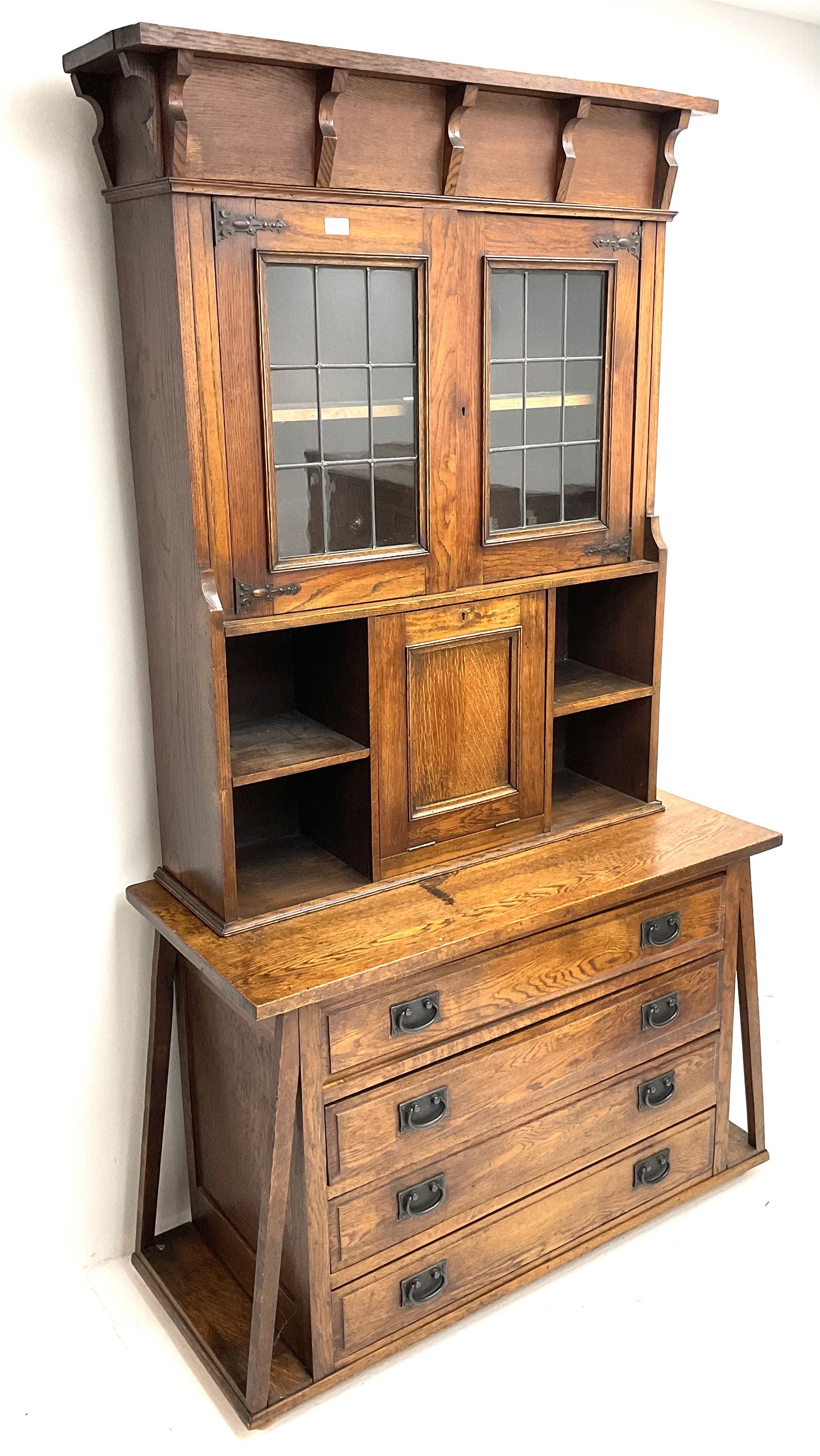 Arts & Crafts oak cabinet on chest, projecting cornice above to lead glazed cabinet doors, two shelves flanking single fall front enclosing fitted interior, four graduating drawers