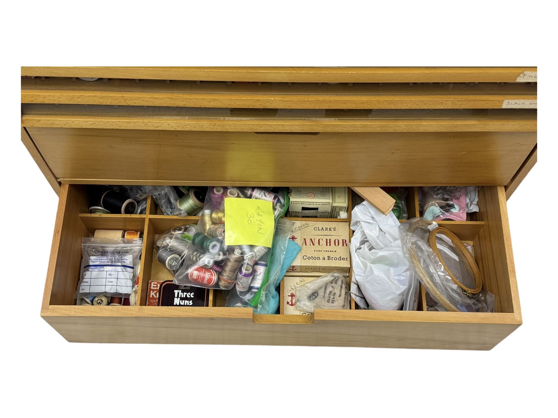 Large beech haberdashery thread storage cabinet, rectangular form with fourteen glass-fronted sloping drawers housing an extensive array of thread spools in assorted colours, over two larger drawers, raised on plinth base