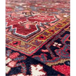 Northwestern Persian Heriz hand-knotted carpet, madder red field with a bold stepped medallion in indigo, ivory, and ivory, surrounded by angular floral motifs and stylized leaves, and the spandrels set within a dark border of rosettes and angular vine motifs, 335cmx252cm