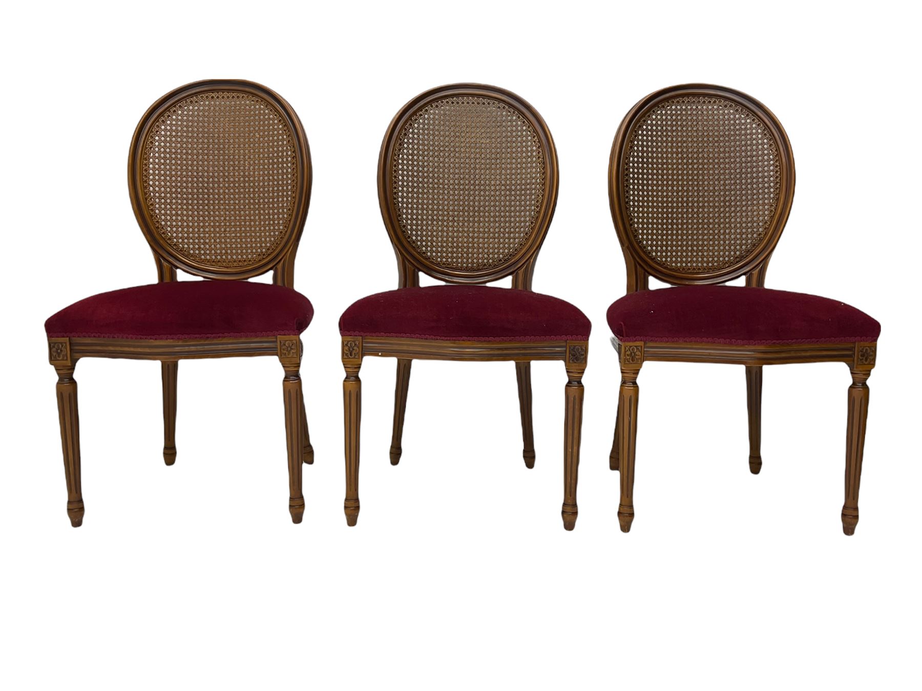Set six French style walnut finish dining chairs, oval cane bergere backs over serpentine seats upholstered in red, flower head carved fluted supports