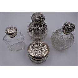 Late Victorian silver mounted glass scent bottle, the body of fluted globular form with pierced scrolling part overlay, and embossed hinged cover lifting to reveal an internal glass stopper, hallmarked Chester 1900, makers mark worn and indistinct, H11.5cm, together with an Edwardian example of similar form, with panelled cut glass body, hallmarked William Neale, Chester 1903, an early 20th century example of facetted oval form, the silver screw threaded cover embossed with a figure amongst blossoming flowers, hallmarked William Comyns & Sons, London 1912, and an early 20th century dressing table jar, the cylindrical octagonal and hobnail cut glass body with silver cover embossed with putti masks, hallmarked S Blanckensee & Son Ltd, Chester, date letter worn and indistinct, D8cm, (4)