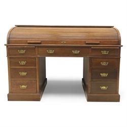 Edwardian oak roll-top desk, the tambour enclosing a fitted interior of pigeonholes and dividers, over a central kneehole flanked by twin banks of drawers with brass handles, on plinth bases