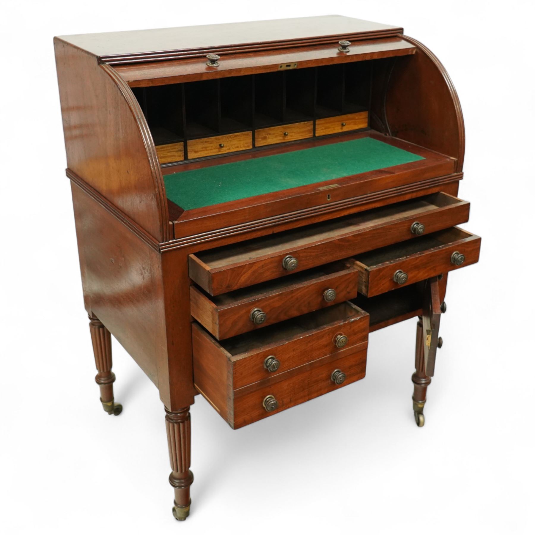 Regency period mahogany cylinder desk, the roll-top enclosing a fitted satinwood interior with pigeonholes and drawers, sliding green baize writing surface, lower section fitted with four drawers and a cupboard, on reeded tapering legs with brass caps and castors