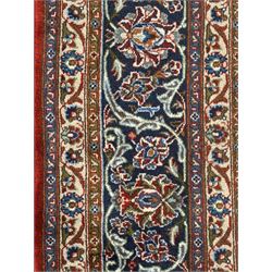 Central Persian Kashan carpet, the red field centred by a large multi-lobed floral medallion, flanked by corner spandrels in navy, enclosed by multiple scrolling floral borders, fringed to two ends