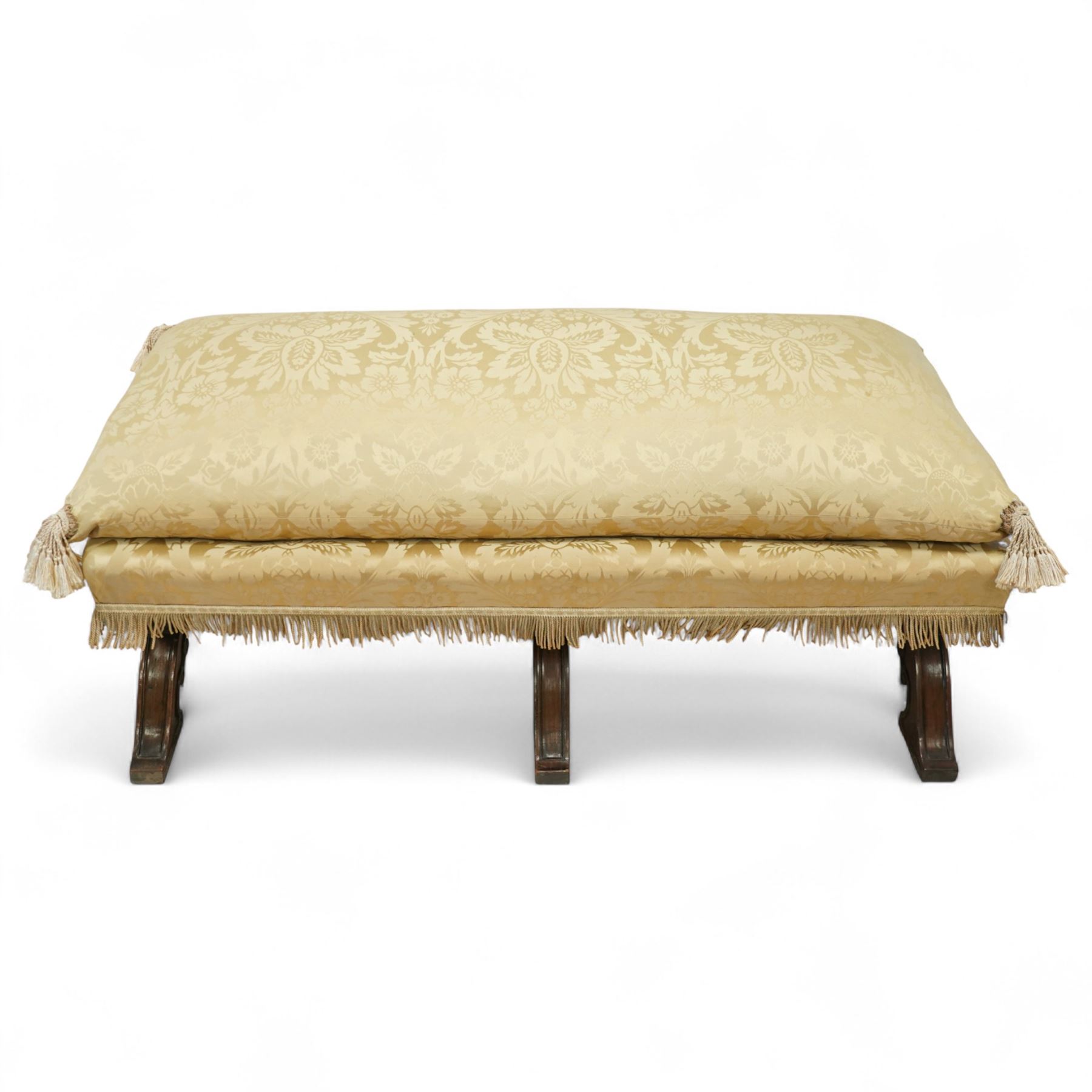 Late Victorian Gothic revival walnut long stool, rectangular padded seat upholstered in cream damask with tasselled corners and fringe border, raised on twin X-frame supports united by a turned stretcher, circa 1880