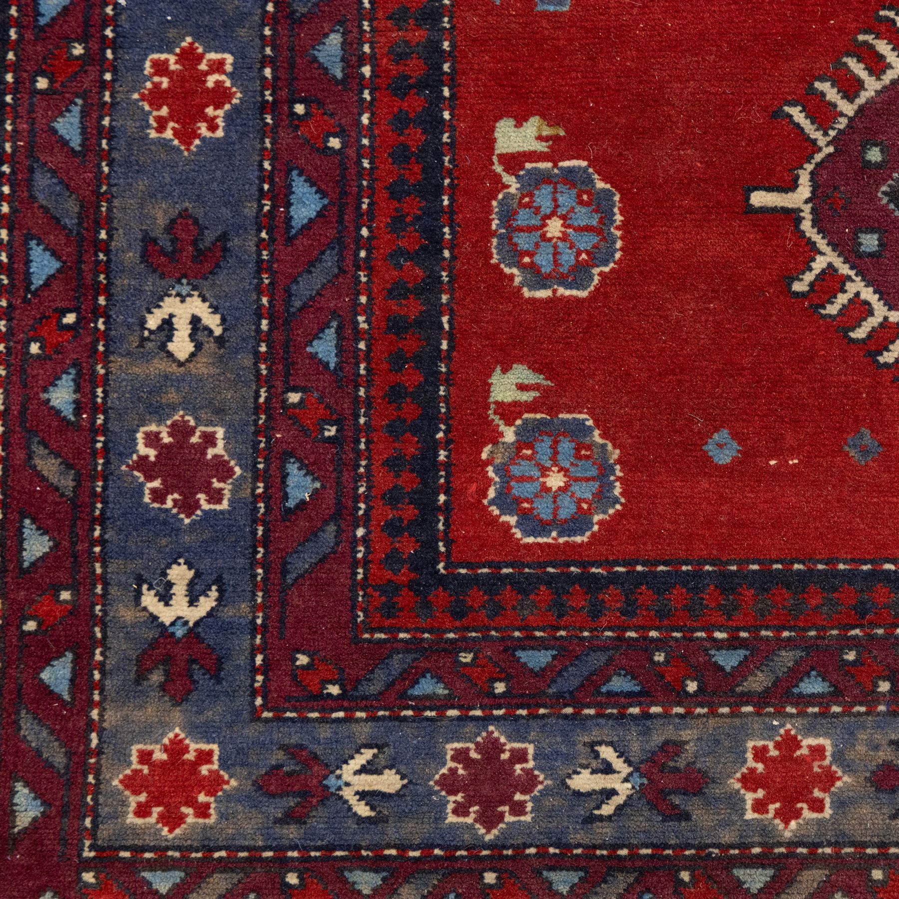 Caucasian Kazak rug, red field decorated with a column of stepped hexagonal medallions in blue, ivory, and crimson, flanked by stylized floral and geometric motifs, enclosed by multiple borders of rosettes and hooked designs 
