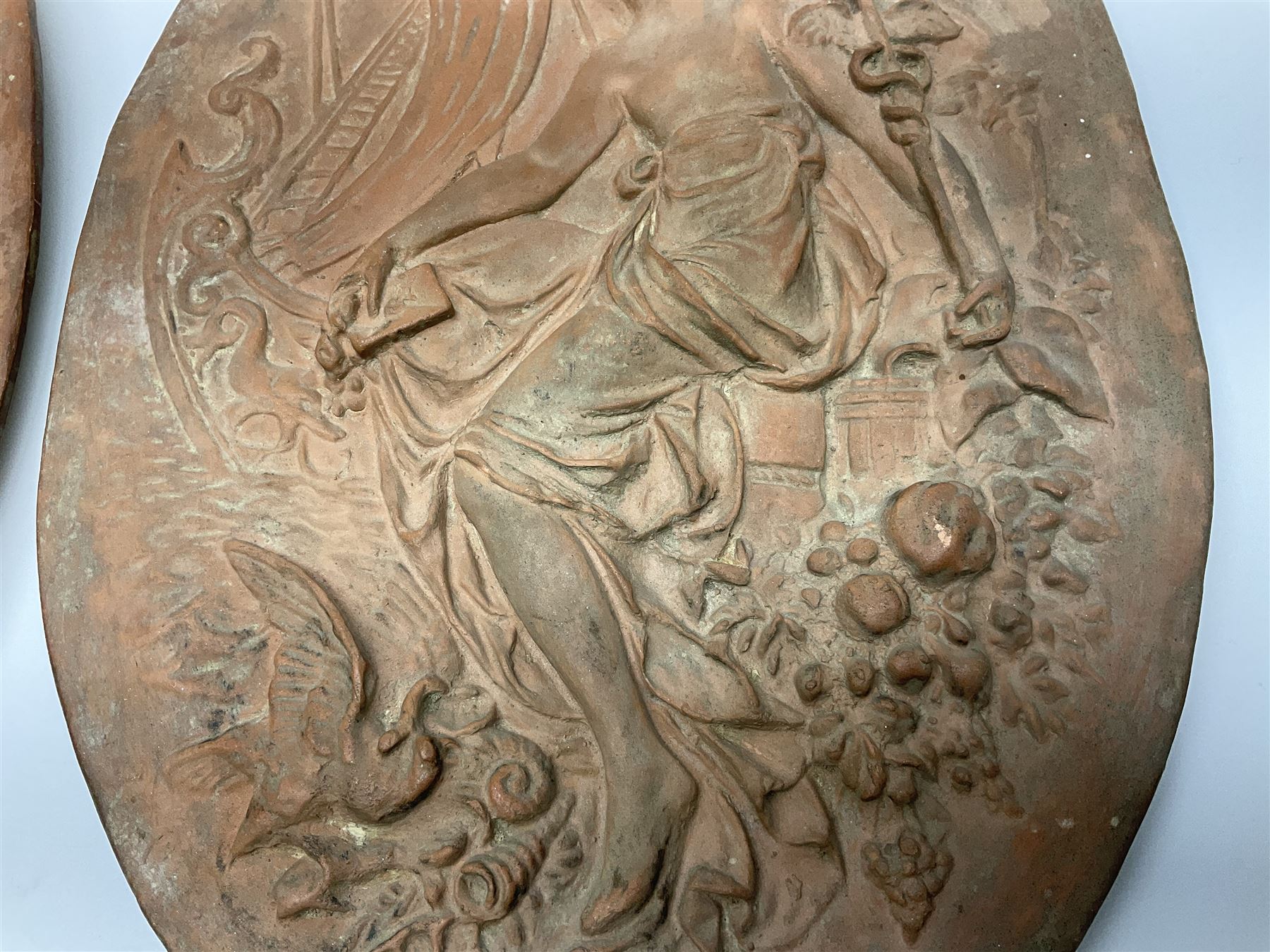 Pair of 19th century classical terracotta relief wall plaques depicting the goddess Hygeia and another goddess, seated holding an ewer, each of oval form, indistinctly signed, each stamped Ferreira verso, H42cm, W30cm