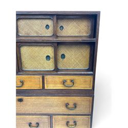 Late Meiji-period Japanese keyaki wood tansu chest, upper section with six sliding woven rattan doors over five drawers, lower section fitted with an asymmetrical arrangement of seven drawers and side cupboard with a hinged door enclosing three additional drawers, iron drop handles to sides