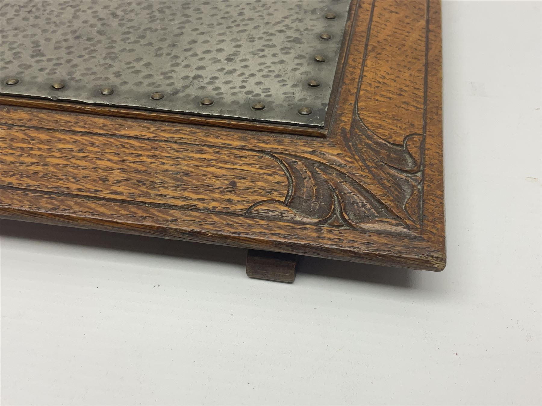 Arts and Crafts oak stand by Arthur Simpson of Kendal, of rectangular form with central hammered pewter panel, surrounded by a border with carved foliate corners, upon two bar supports, bearing label detailed 