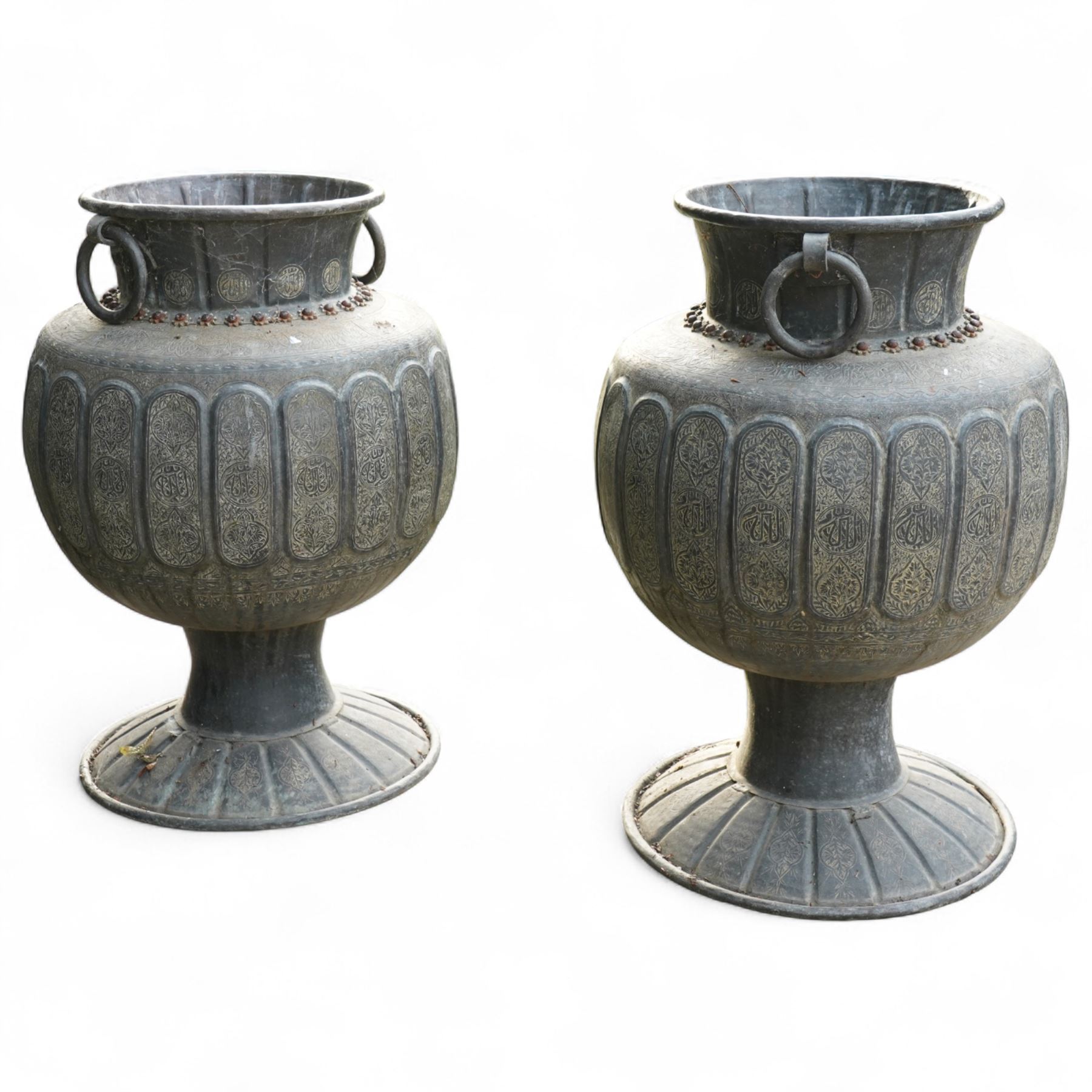 Pair of large Indian cast metal garden urns, each of bulbous form with engraved foliate and script panels, twin ring handles to the neck, raised on fluted pedestal bases
