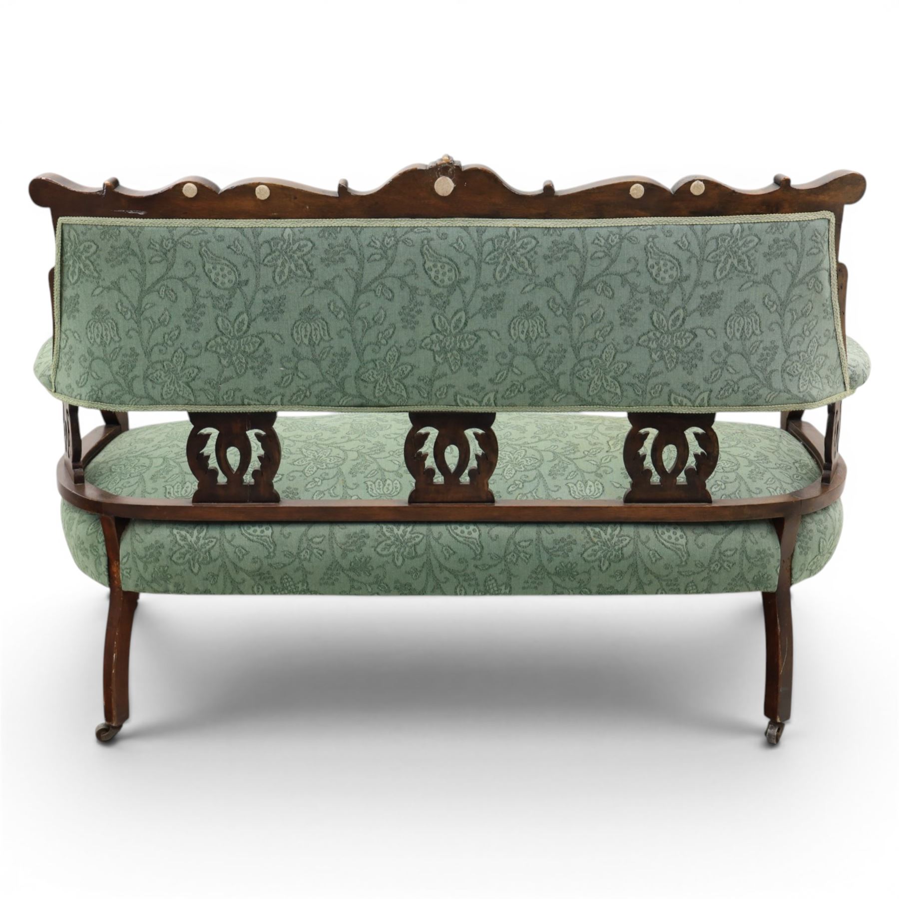 Edwardian mahogany framed sofa, shaped cresting rail with scroll terminals and carved foliate pediment, upholstered back and swept arms in green foliate fabric, pierced splat supports, serpentine front seat rail, on cabriole supports terminating in castors