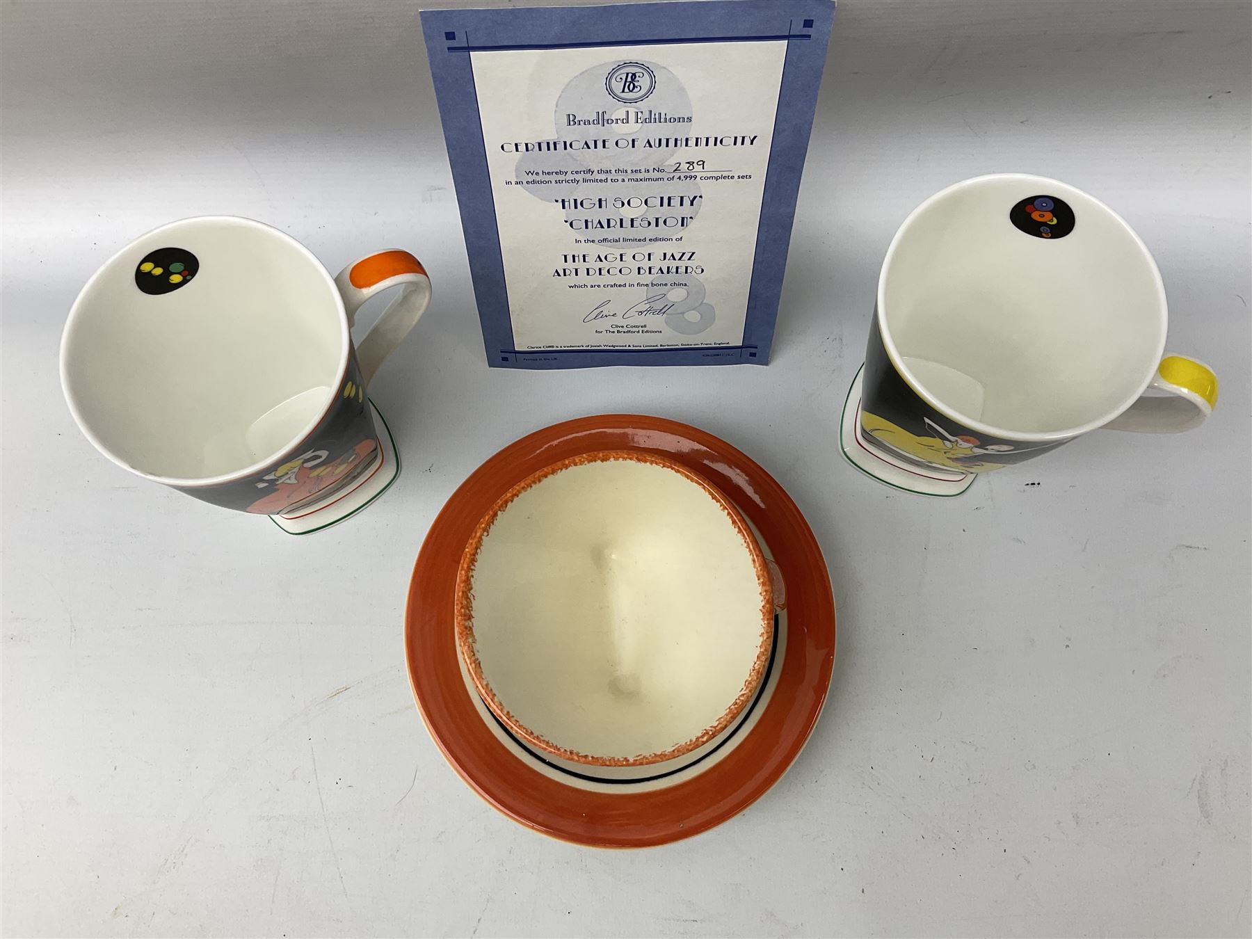 Two limited edition Bradford Exhange Clarice Cliff Age of Jazz beakers, no 289/4,999, with certificate, in box, together with a Moorland Art Deco Clarice Cliff style Huntley Cottage pattern teacup and saucer 
