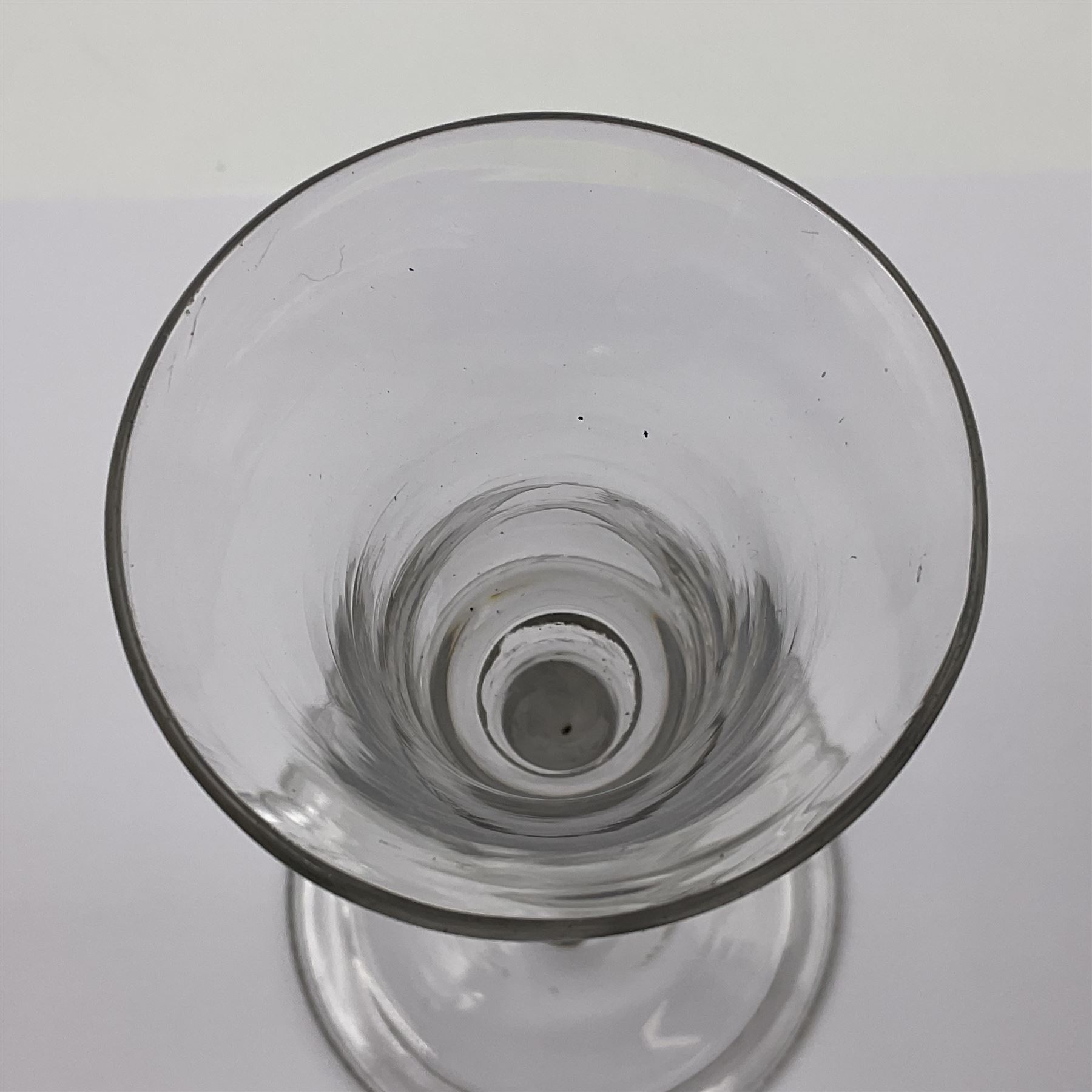 Three 18th century wine glasses comprising a plain stemmed glass with bell shaped bowl and conical folded foot H16cm, another plain stemmed glass with ogee bowl and folded foot and a Continental glass with gilt faceted bowl, decorated with male figure within a landscape, on a clear Silesian seven sided cut stem (3)