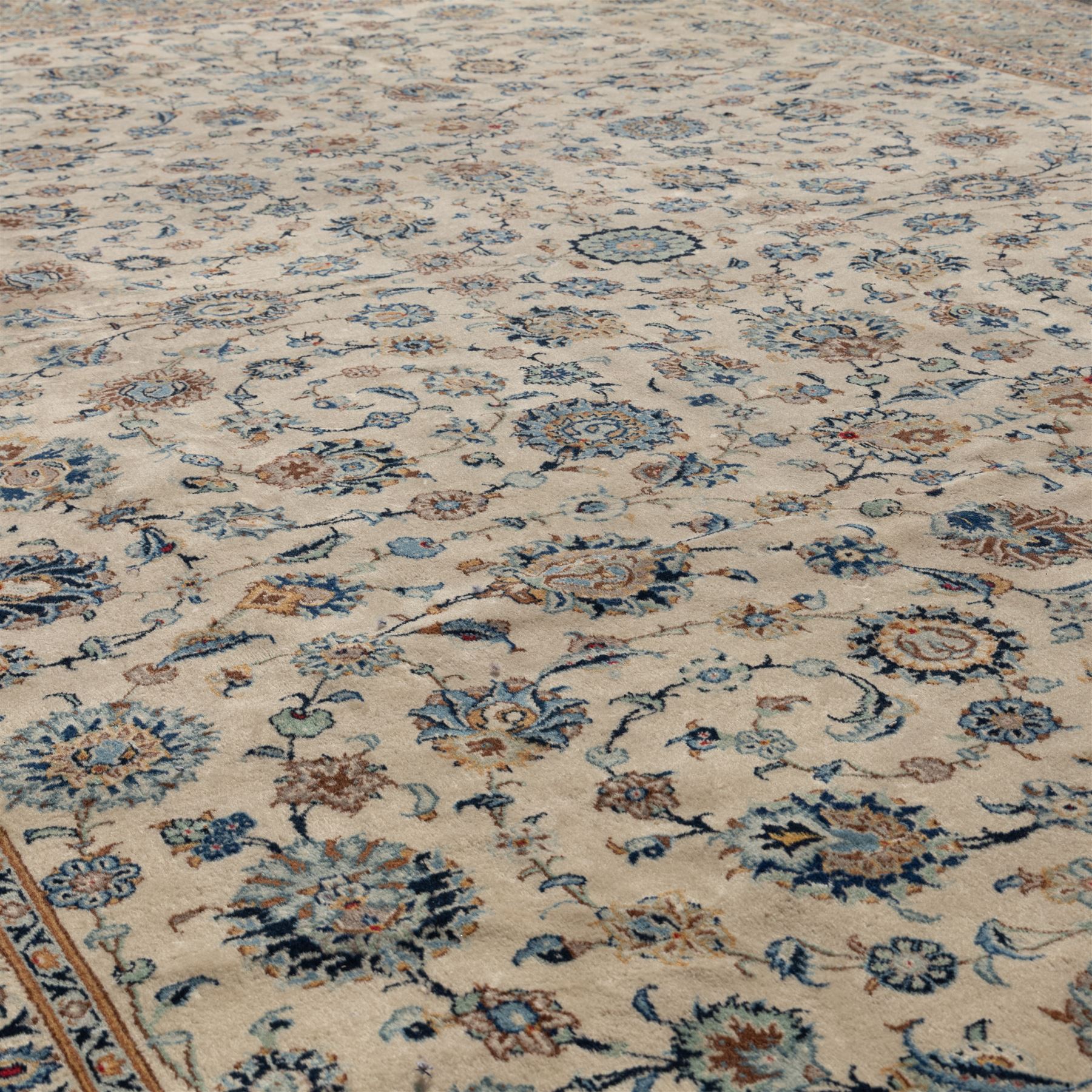 Large Central Persian Kashan hand-knotted carpet, ivory field with small central floral medallion issuing an all-over design of palmettes, rosettes, and scrolling vines enclosed by a complimentary foliate border framed by guard stripes, in a palette of ivory, power blues, and muted polychrome tones, with cotton fringe ends 