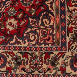 Central Persian Isfahan hand-knotted rug, madder red field, with elaborate central medallion with pendants and scrolling arabesques, palmettes and stylized floral sprays arranged in a densely ornamented ground of classical Safavid inspiration, ivory border with a continuous vine scroll of palmettes and rosettes, flanked by multiple guard stripes in navy and red with geometric and floral motifs, with cotton fringe ends 