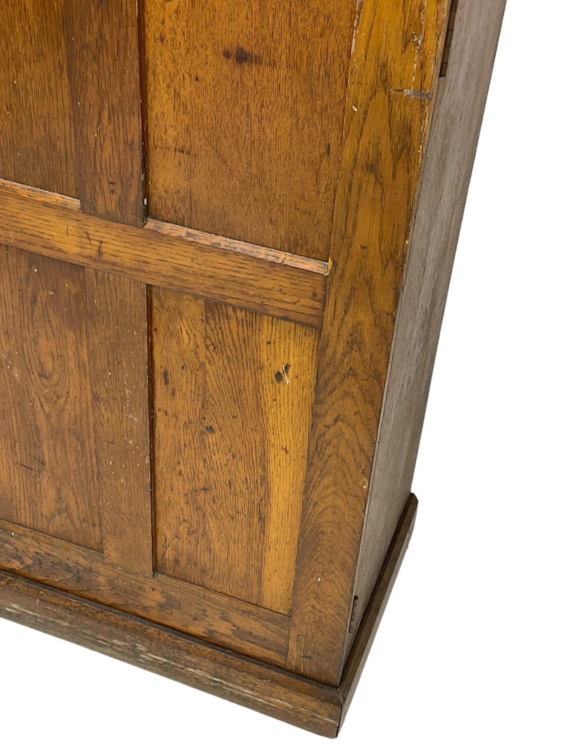 The North of England School Furnishing Company Limited Darlington - early 20th century oak school cupboard, projecting moulded cornice over two panelled doors, fitted with shelves, on chamfered plinth base 