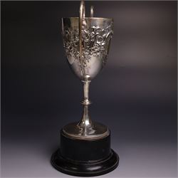 Edwardian silver twin-handled trophy, with embossed floral and scrolling decoration, upon a knopped stem and circular foot, hallmarked Goldsmiths & Silversmiths Co Ltd, London 1903, upon a black plinth, including plinth and handles H32cm