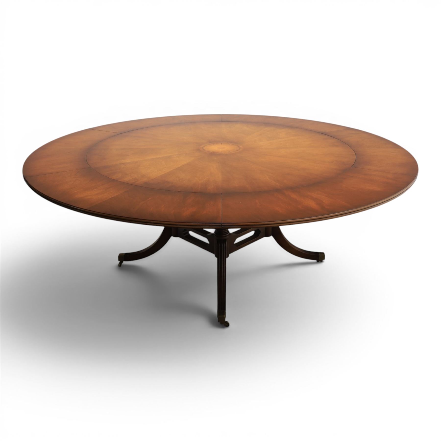 Bevan Funnell Reprodux - Regency design mahogany extending dining table, circular radial veneered top with central fan inlaid patera, on turned pedestal with four reeded downswept supports terminating in brass caps and castors, with six addtional leaves in a fitted storage case