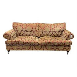 Duresta - pair of Grande three-seat sofas, traditional shaped with rolled arms and upholstered loose cushions, in red ground fabric with raised gold foliate pattern, on turned feet with brass castors 