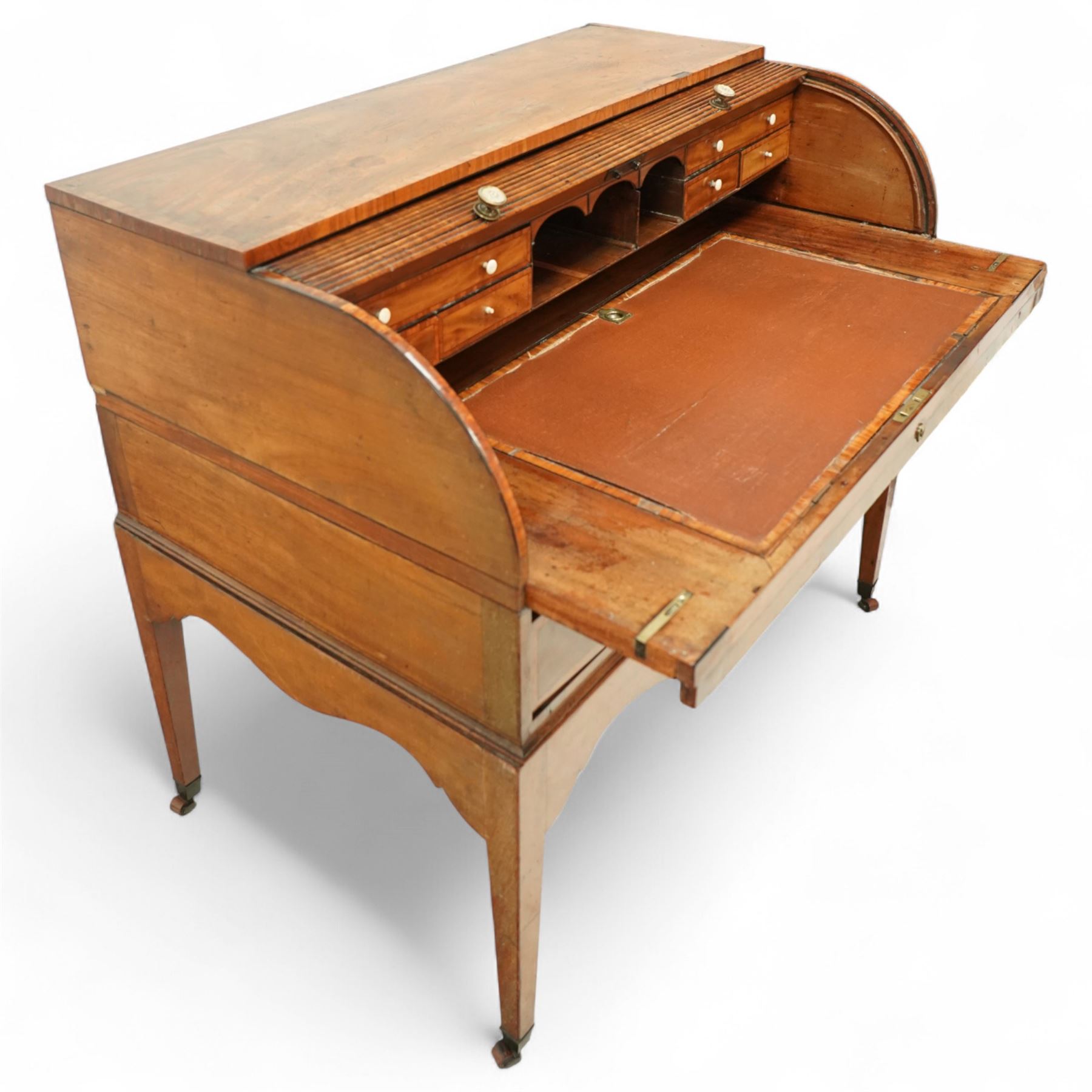 George III mahogany cylinder front writing desk, the hinged tambour enclosing pigeonholes and drawers with bone handles, sliding writing surface with leather inset, three frieze drawers below, on square tapering legs with brass caps and castors
