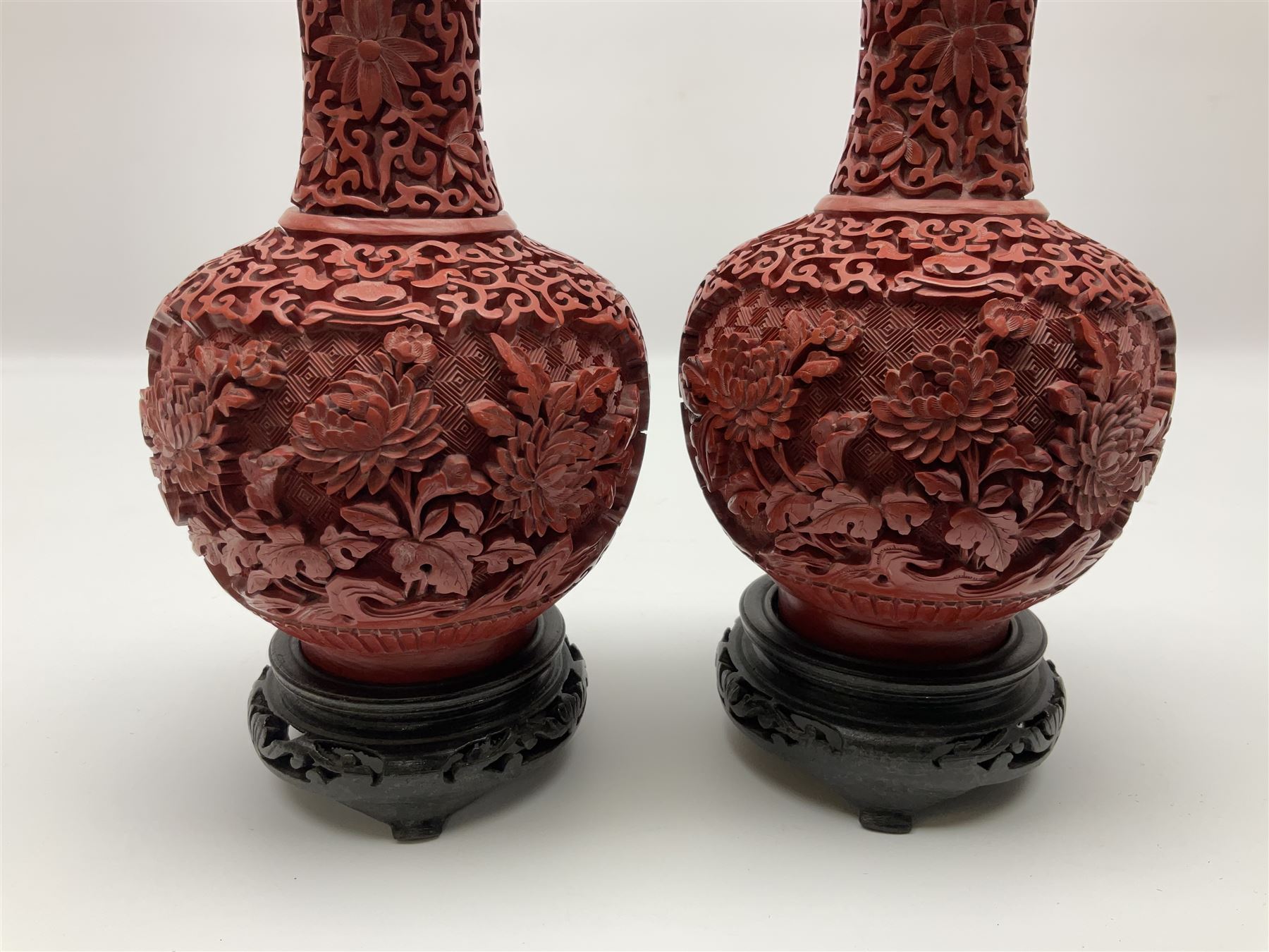 Pair of Chinese cinnabar lacquer vases, each of bulbous baluster form, carved with peonies and foo dogs amongst scrolls, with blue enamel interior and upon wooden bases, H20cm