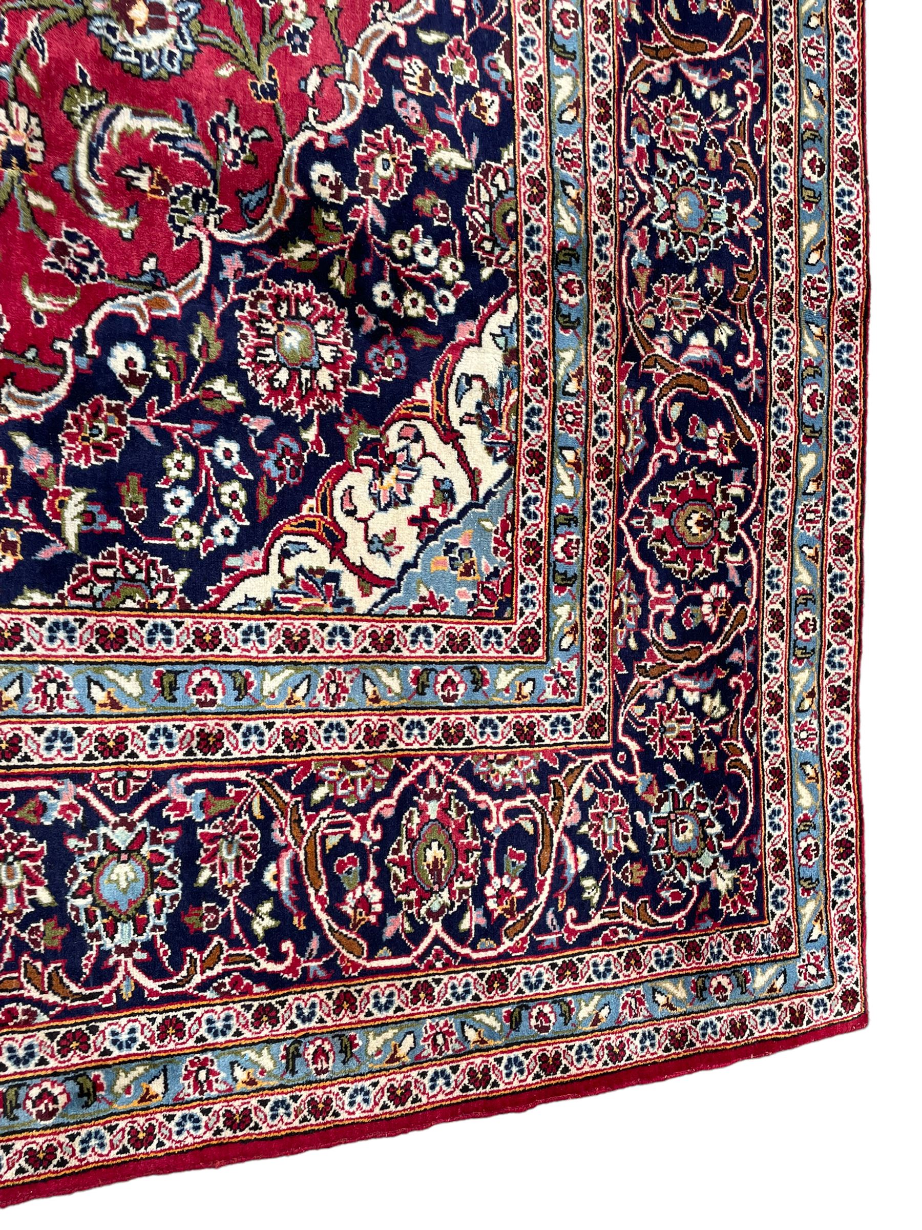 Central Persian Kashan crimson ground carpet, central  floral pole medallion with matching spandrels within a field of scrolling palmette motifs and foliage, the heavily banded indigo border with repeating plant motifs interlaced with scrolled branches